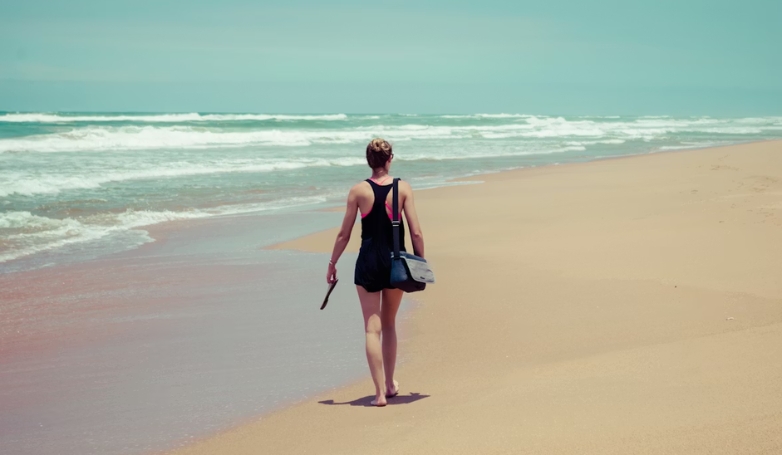 A woman walks along Union Beach in Siargao, carrying a bag, enjoying the scenic coastal view.